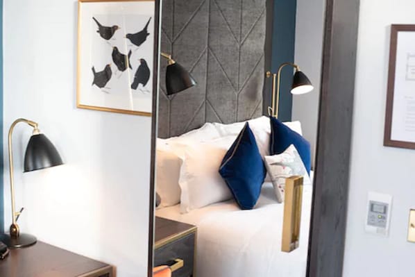 Un dormitorio con cama, lámparas de noche, un cuadro enmarcado con pájaros e iluminación en la pared.