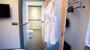 A hotel bathroom with a shower, toilet, and a towel rack with robes.
