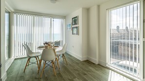 Et moderne spiseområde med et rundt bord, hvide stole og udsigt over byen gennem store vinduer.