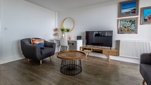En moderne stue med en grå sofa, et rundt sofabord, et fjernsyn og billeder i rammer på væggen.