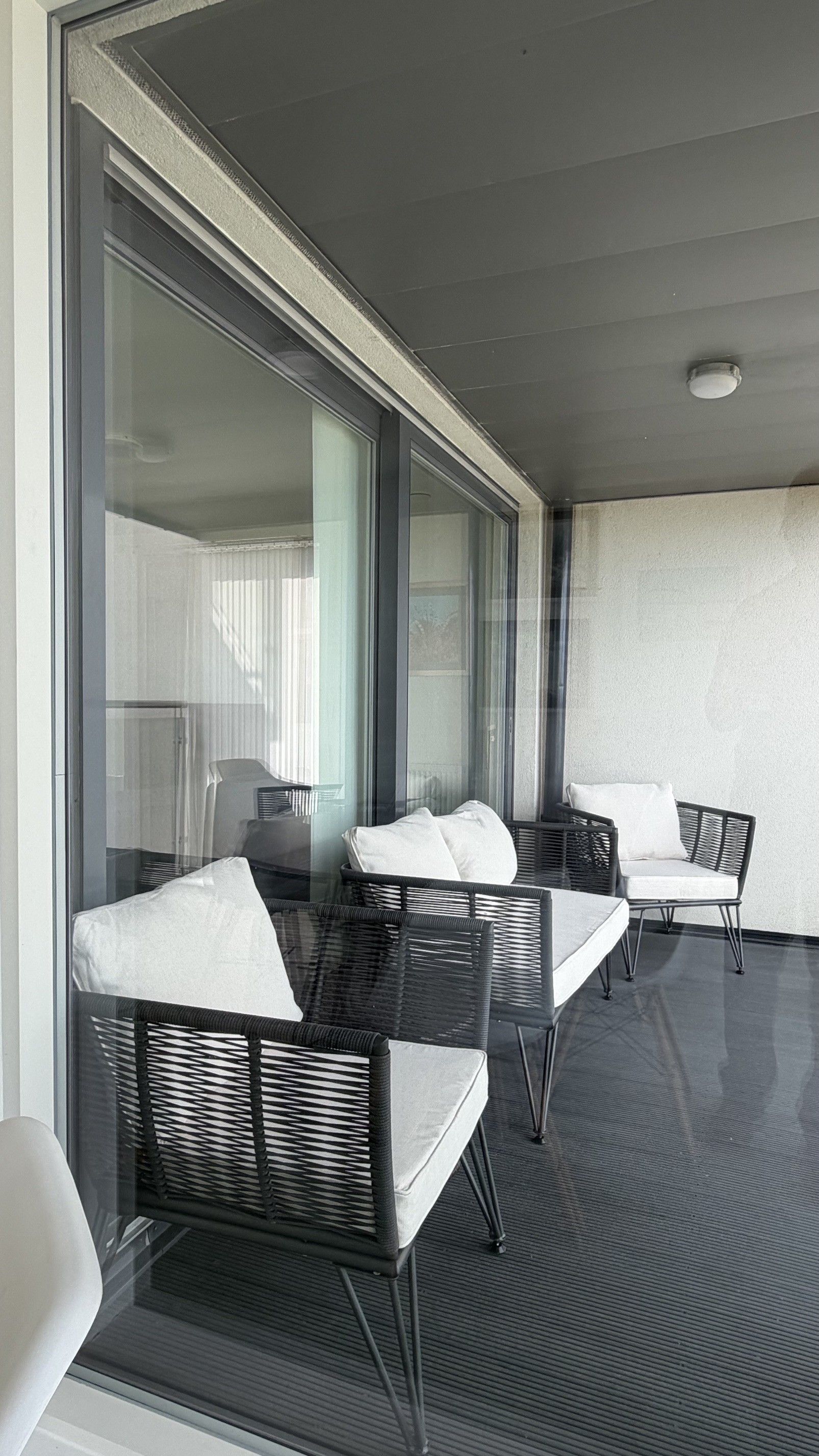 A balcony with wicker furniture, a glass door, and a ceiling light.
