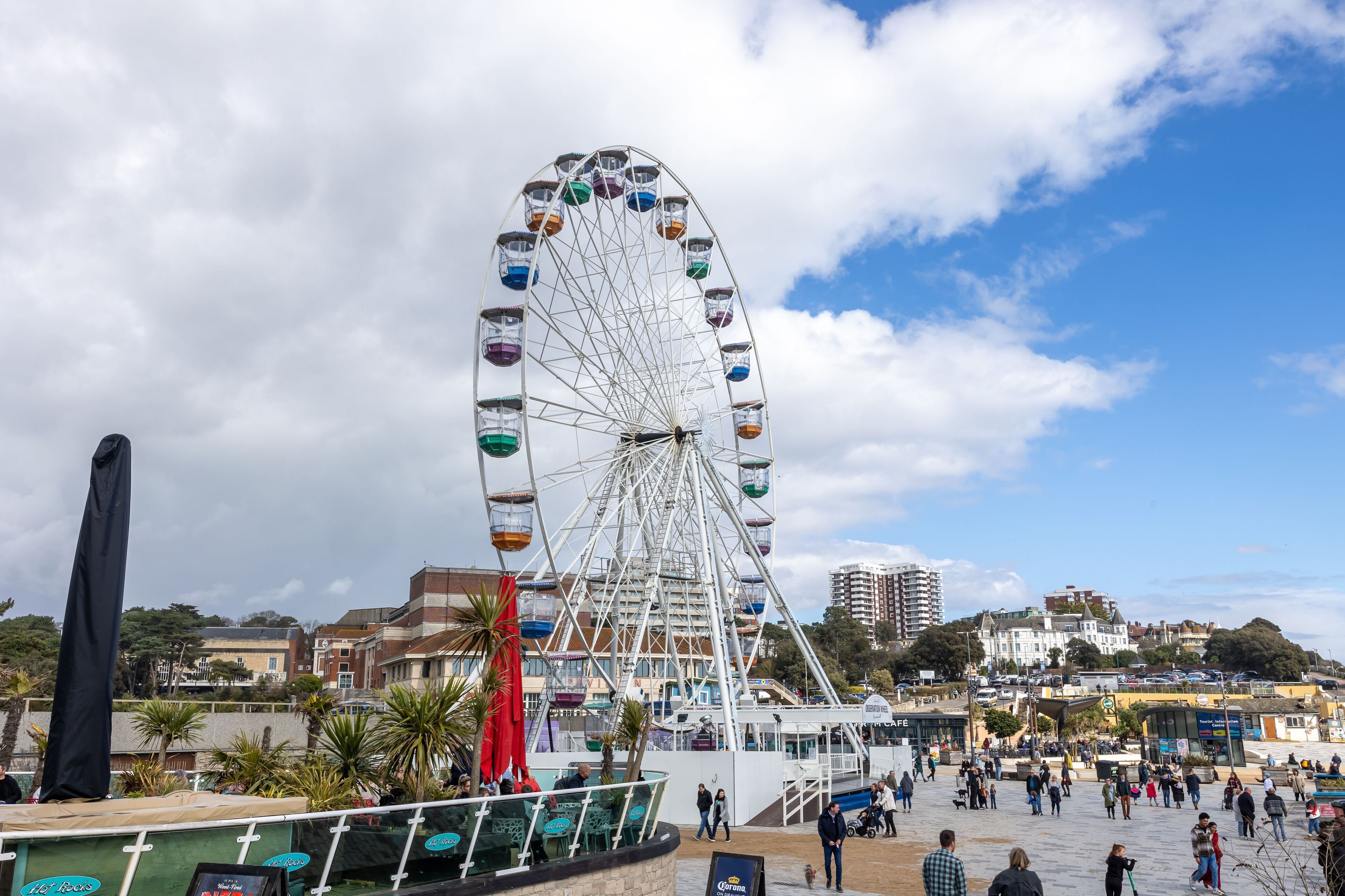 A Ferris wheel with multiple cabins, surrounded by a plaza with people and buildings in the background.