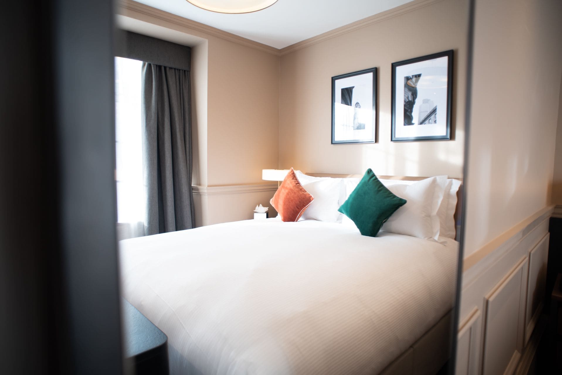 A hotel room with a large bed, a nightstand, a window with curtains, and two framed pictures on the wall.