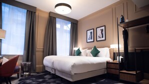 A hotel room with a large bed, a desk with a lamp, a chair, and a wardrobe.