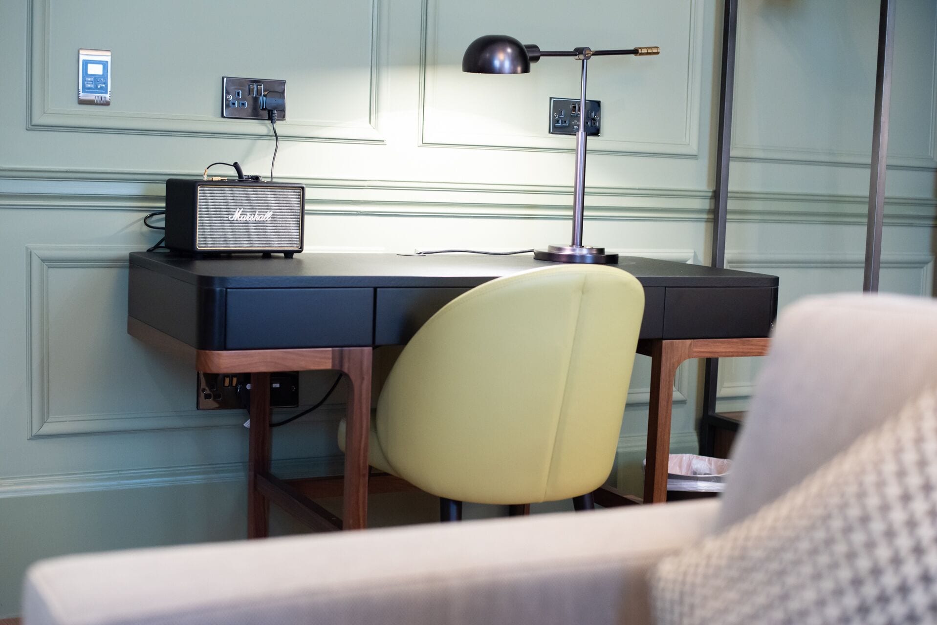 A hotel room with a desk, a chair, a lamp, and a radio.