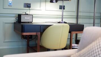 A hotel room with a desk, a chair, a lamp, and a radio.
