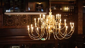 A chandelier with multiple candle-like lights, a bar area with a counter and framed pictures, and ornate wooden paneling.