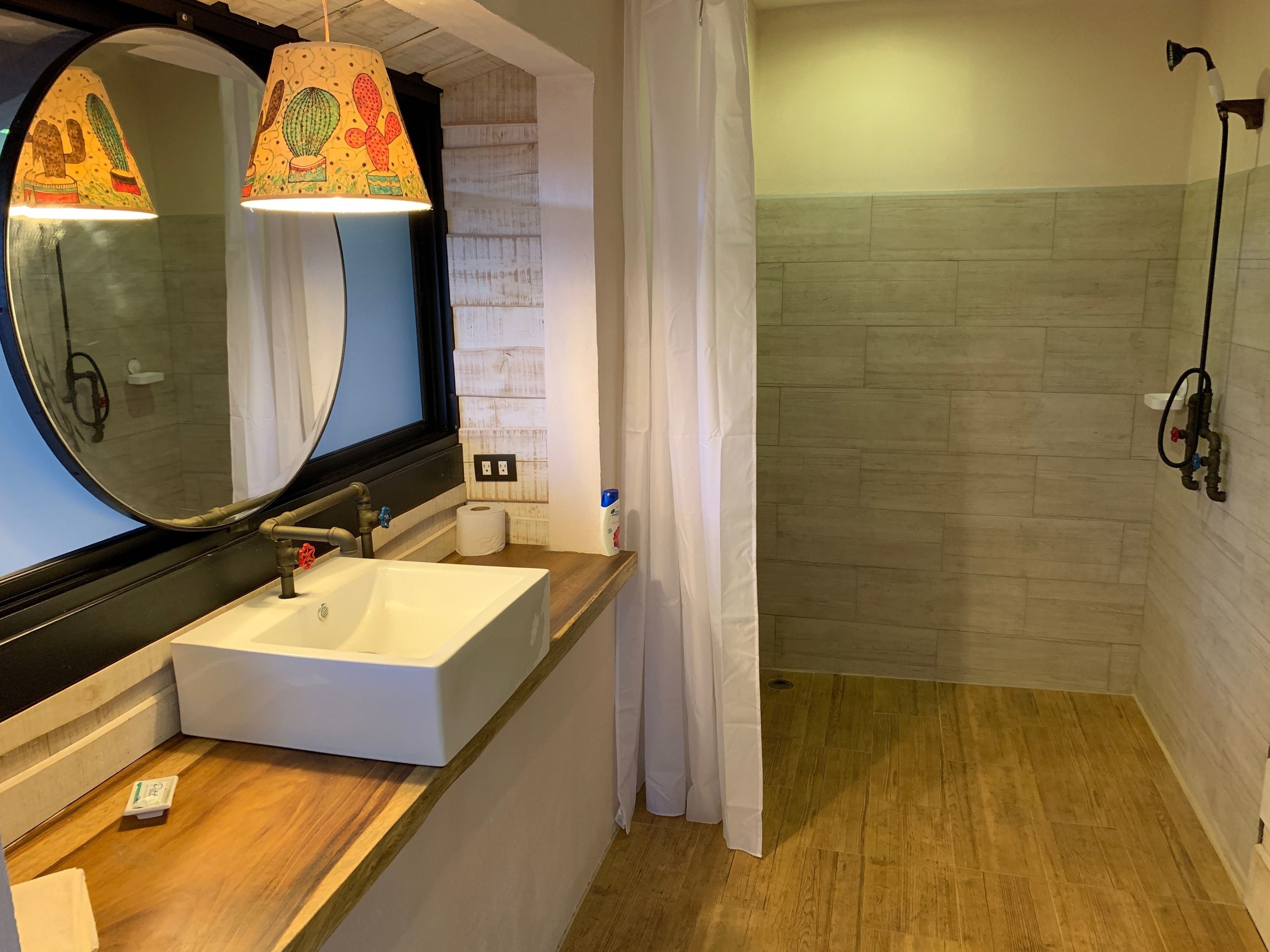 Een badkamer met een houten wastafelmeubel, een grote spiegel, een wastafel, een douche met gordijn en een handdoekhouder.
