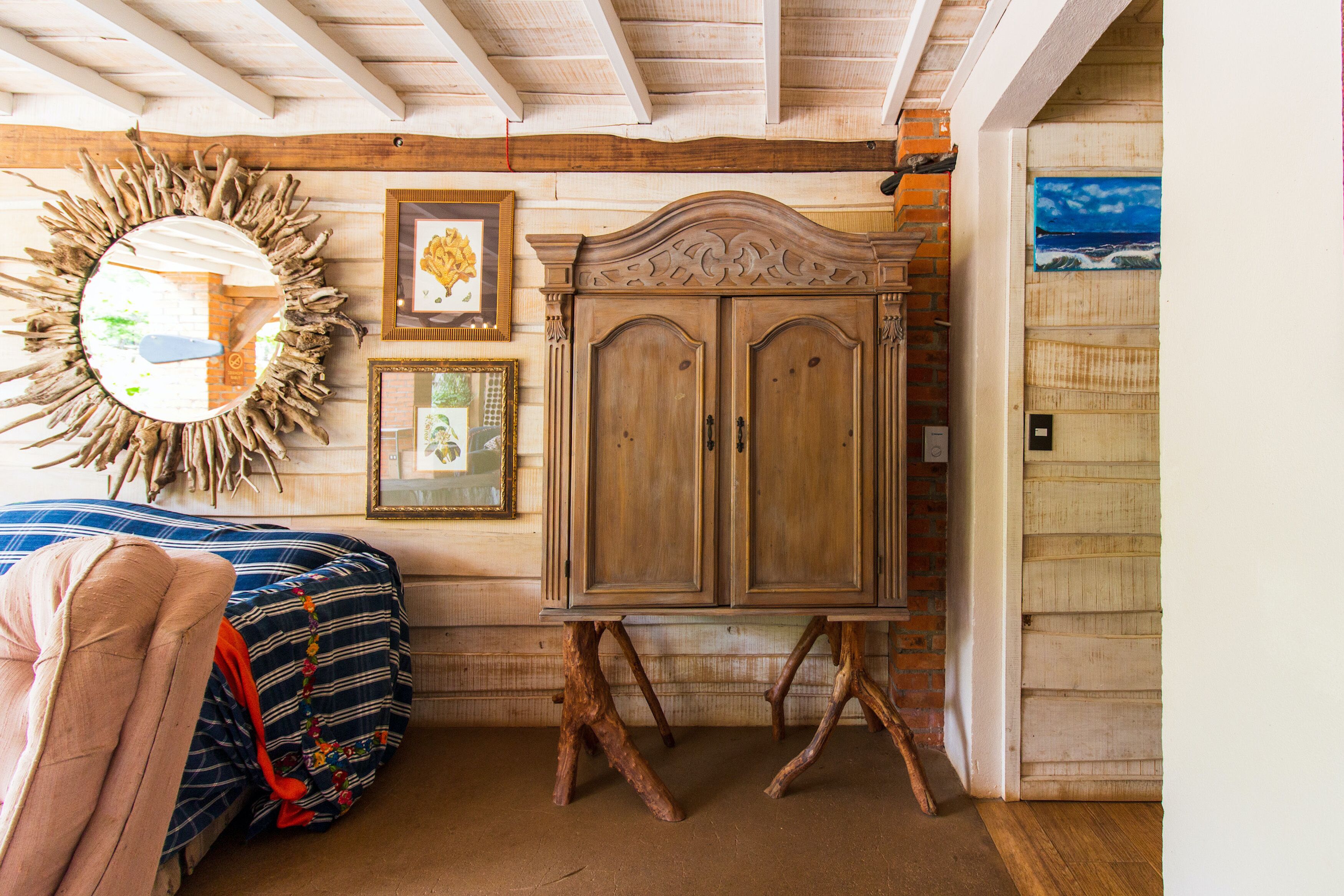 Une chambre avec une armoire en bois, un miroir avec un cadre sobre, et un lit recouvert d’une couverture aux couleurs vives.
