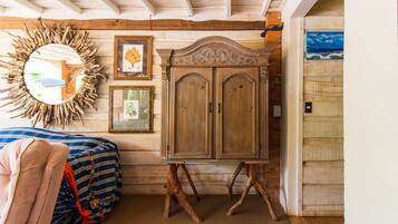 Une chambre avec une armoire en bois, un miroir avec un cadre sobre, et un lit recouvert d’une couverture aux couleurs vives.