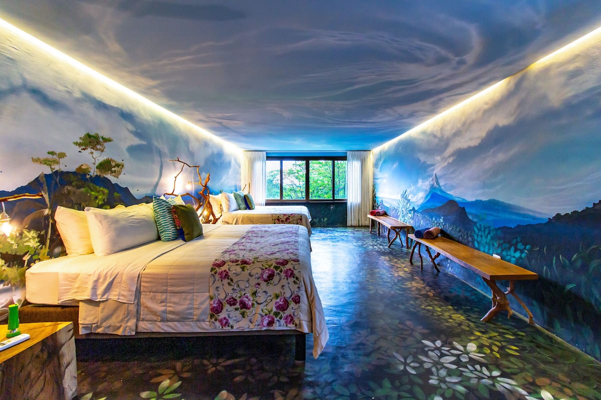 A room with a bed, a bench, and a mural on the walls.