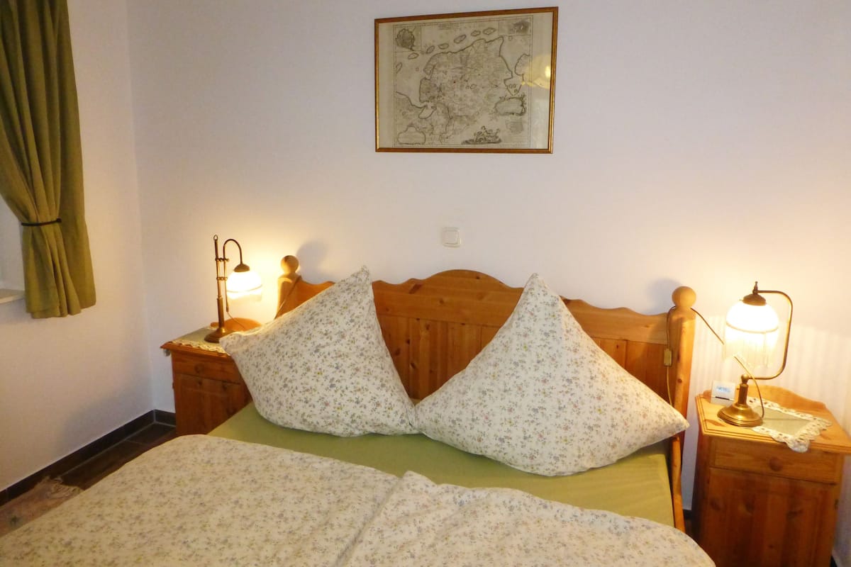 Ein Schlafzimmer mit einem Holzkopfteil, floralem Bettzeug, zwei Nachttischlampen und einer Karte an der Wand.