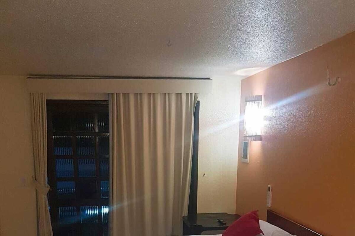 A hotel room with a large bed, red and white bedding, a nightstand, and a window with curtains.