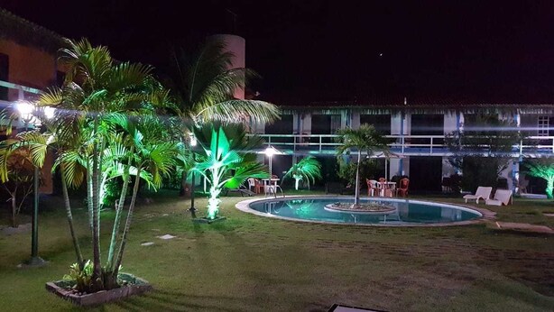 Vista nocturna de un patio de hotel con piscina, palmeras y mobiliario exterior.