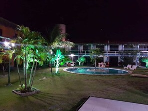 A nighttime view of a hotel courtyard with a swimming pool, palm trees, and outdoor seating. - Hotel Cumbuco Praia (Caucaia)