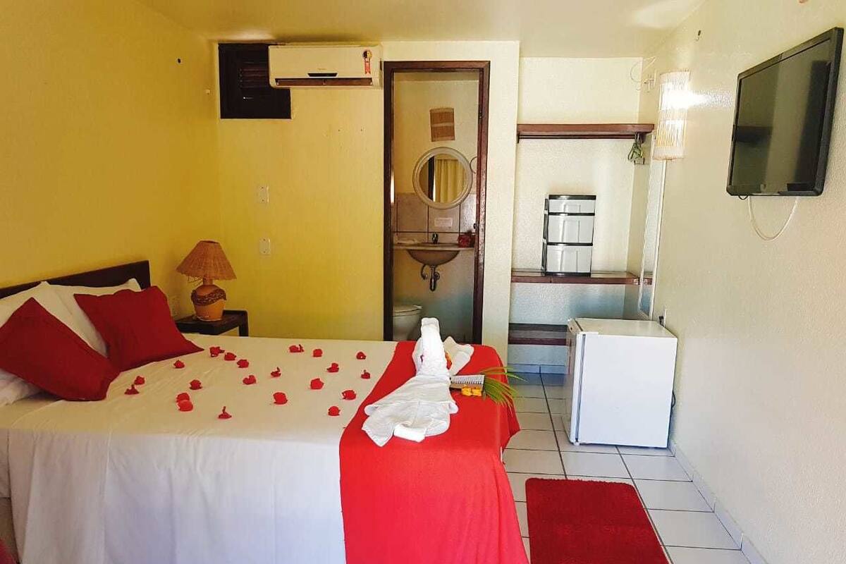 A hotel room with a bed, a small kitchenette, a mirror, and a TV.