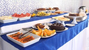 Una mesa de buffet con diversos alimentos, entre ellos frutas, pasteles y un pastel de chocolate.