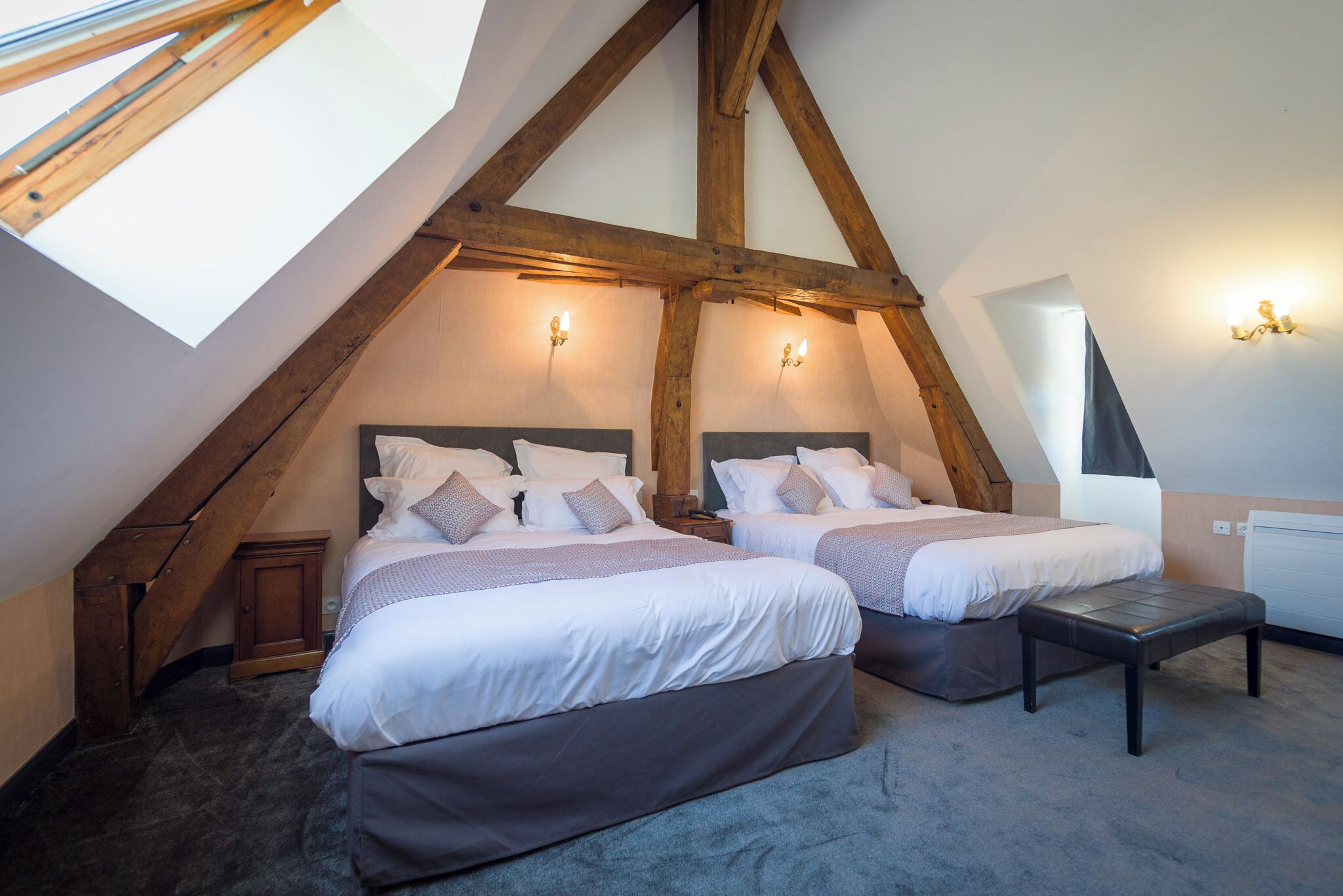 Ein Schlafzimmer mit zwei Betten, Holzbalken, Dachfenster und Wandleuchten.