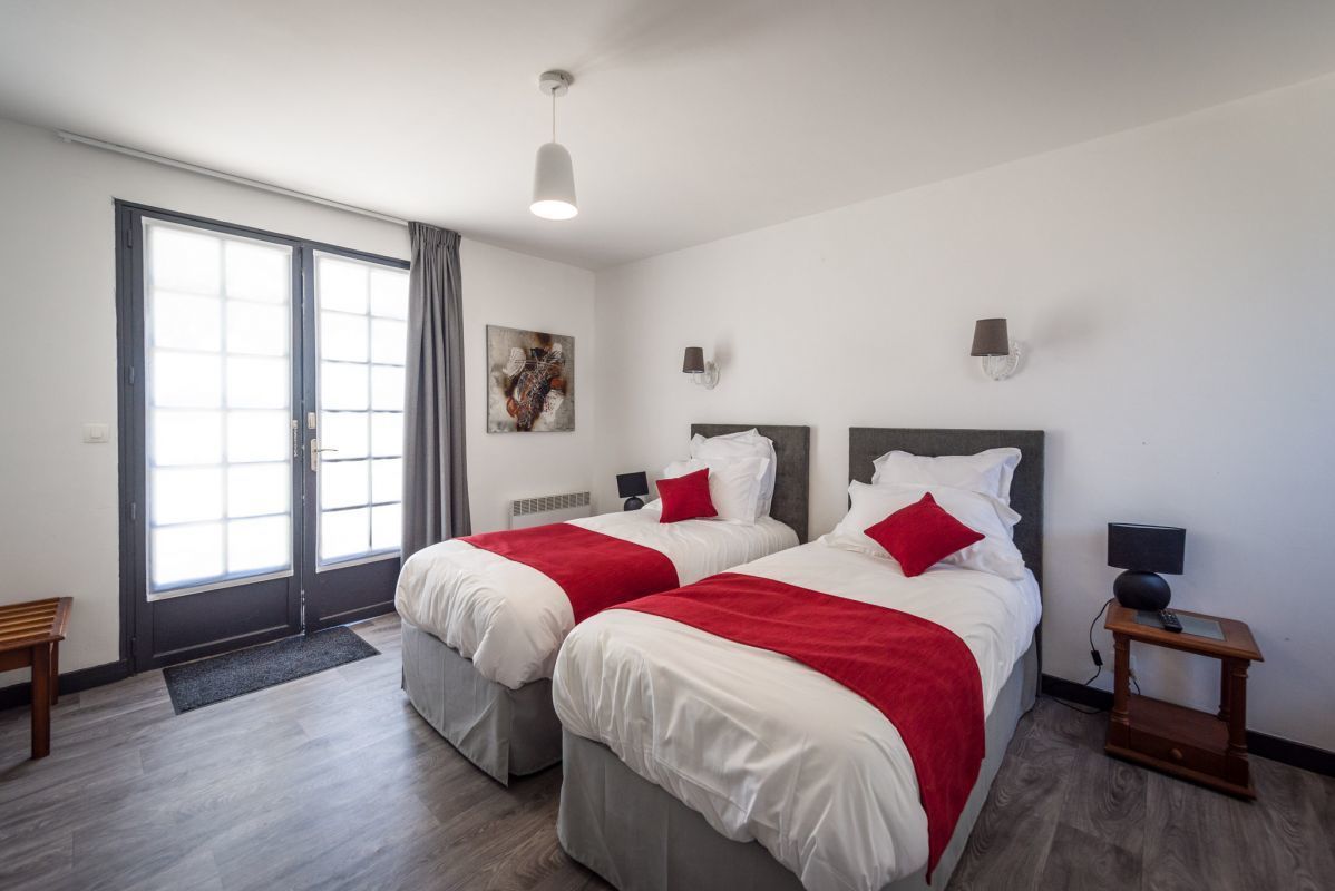 Hotelkamer met twee bedden, een bureau, een stoel, een bureaulamp, een nachtkastje en een schilderij aan de muur.