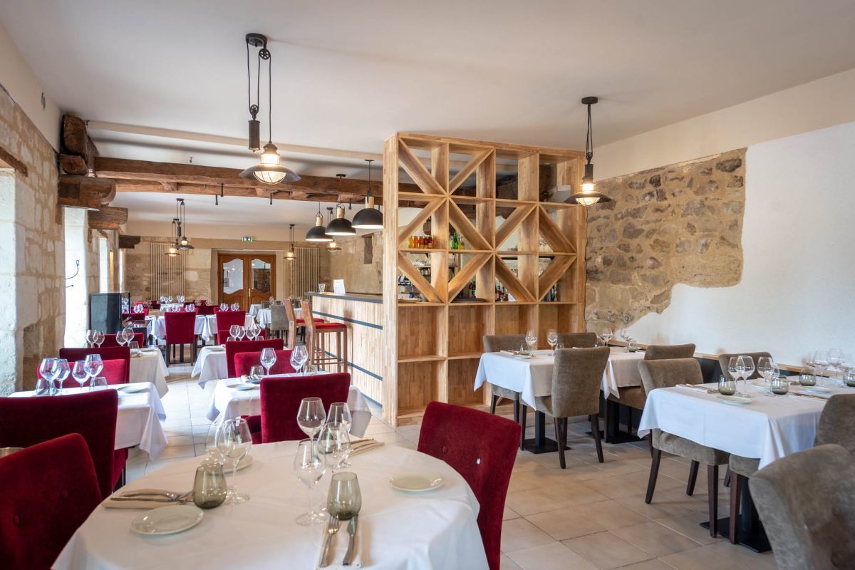 Een restaurant met gedekte tafels, houten balken in het plafond en stenen muren.