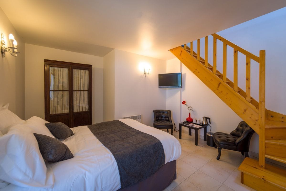 A bedroom with a large bed, a wooden staircase, a TV mounted on the wall, and a small table with a vase.