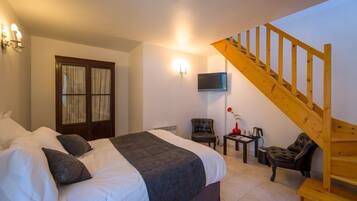 A bedroom with a large bed, a wooden staircase, a TV mounted on the wall, and a small table with a vase.