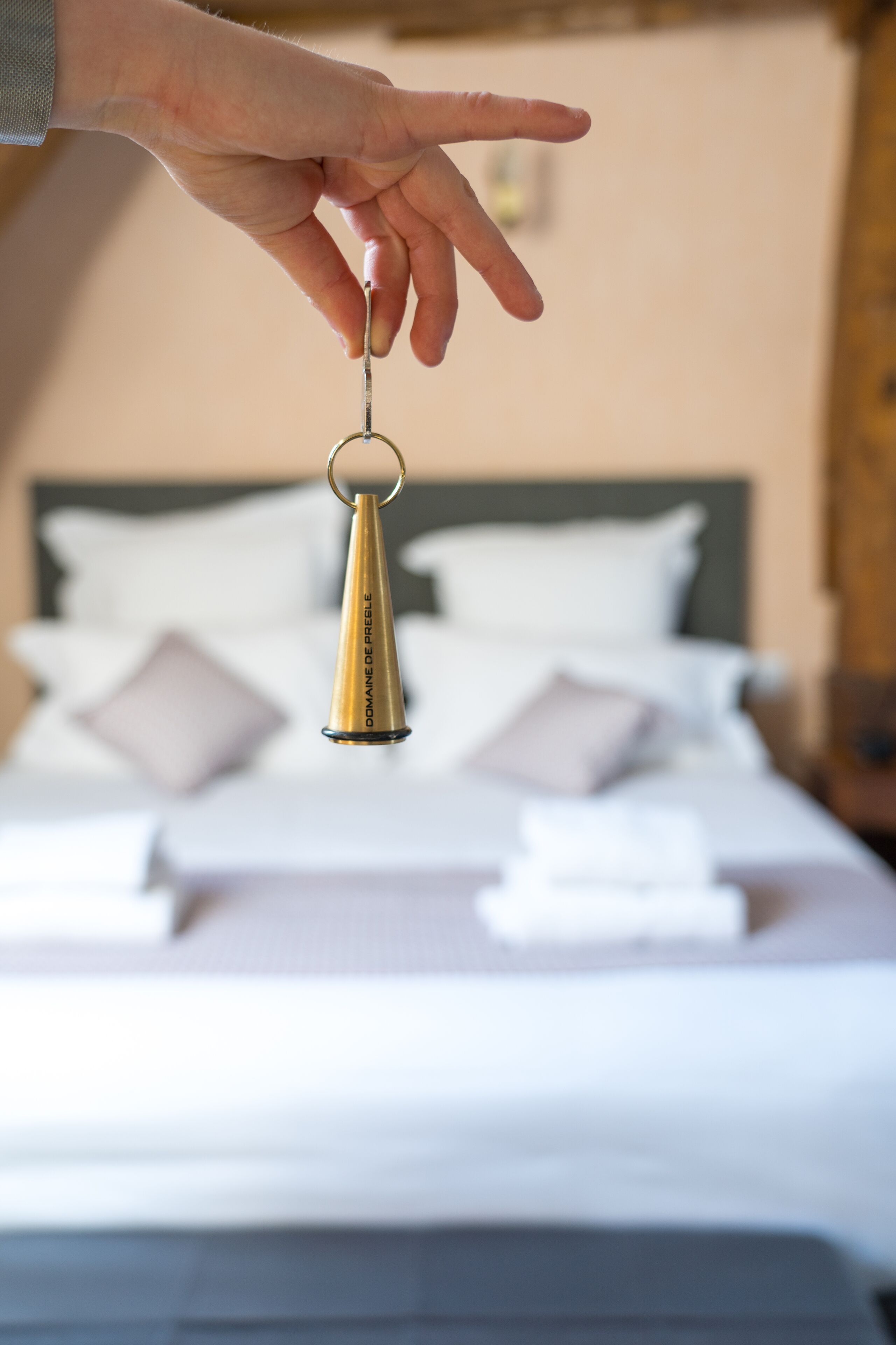 Une main tenant un porte-clés avec une clochette, devant un lit avec une literie et des oreillers blancs.