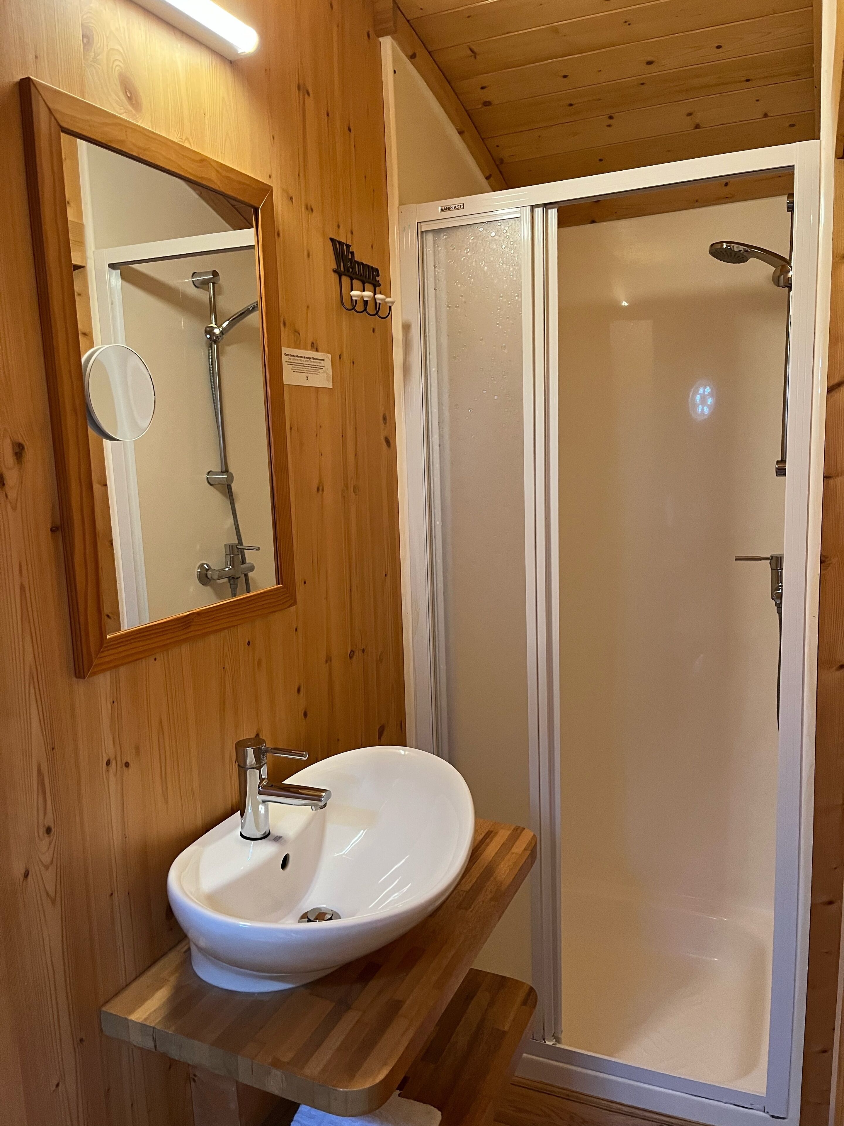 Une salle de bain aux murs lambrissés, avec un lavabo blanc, un miroir et une douche à parois de verre.
