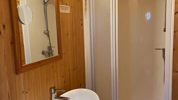Un baño con paneles de madera, un lavabo blanco, un espejo y una ducha con mampara de vidrio.