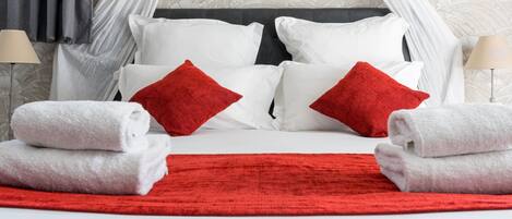 A neatly made bed with white and red pillows, a red throw blanket, and white towels.