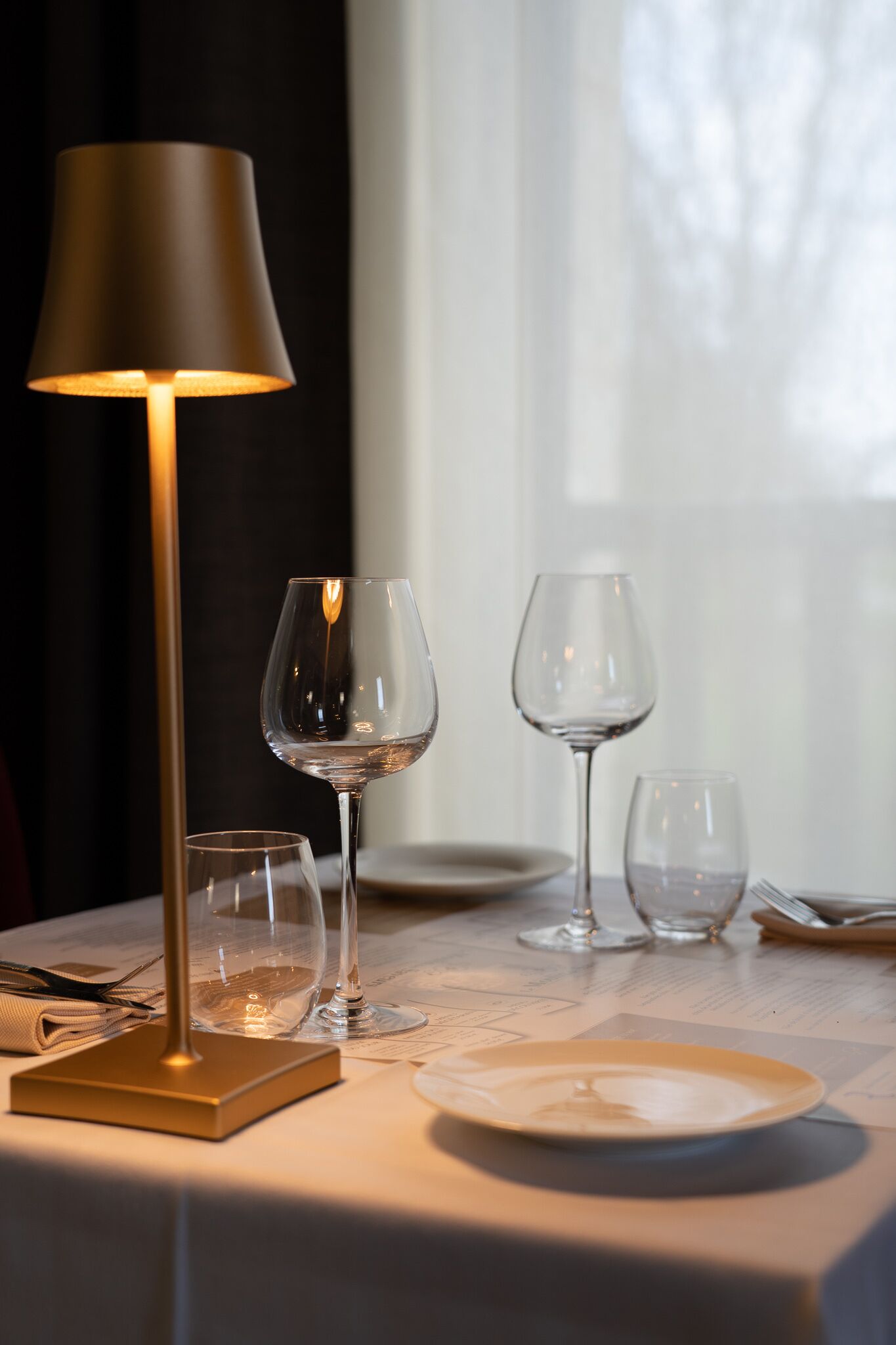 Een tafel met een lamp, wijnglazen en een bord, wat wijst op een eettafel.