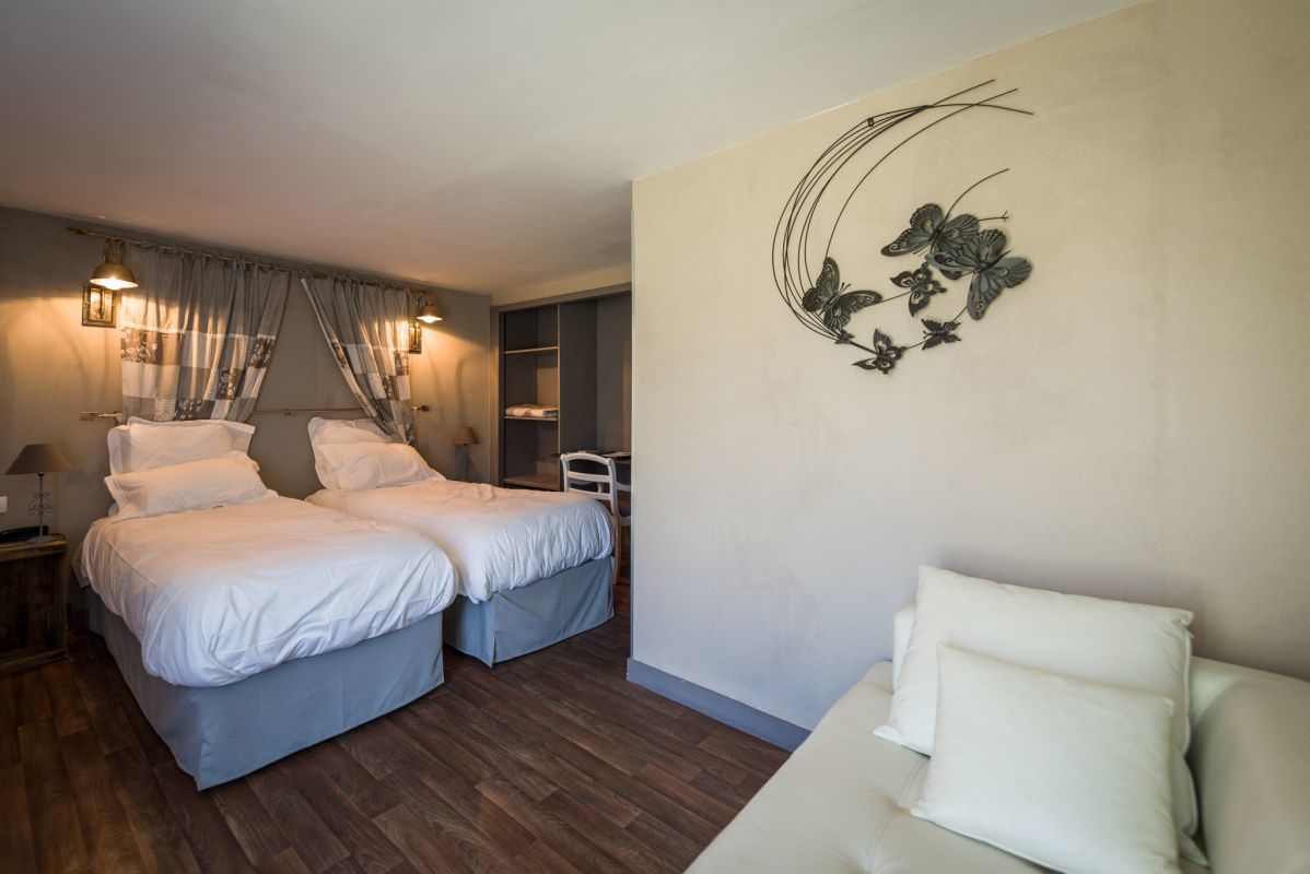 Habitación de hotel con dos camas, un sofá, un cuadro decorativo y una mesita de noche con lámpara.
