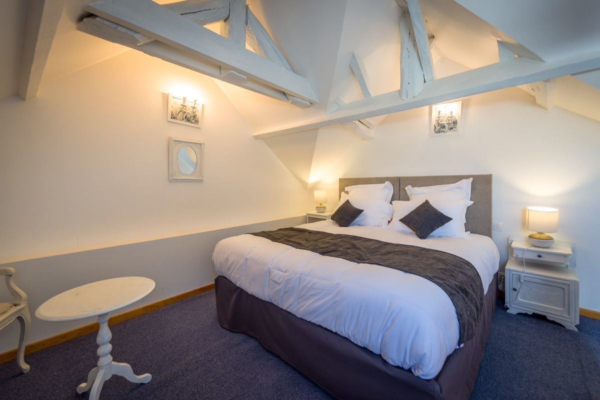 A bedroom with a bed, bedside tables, a small round table, and exposed wooden beams on the ceiling.