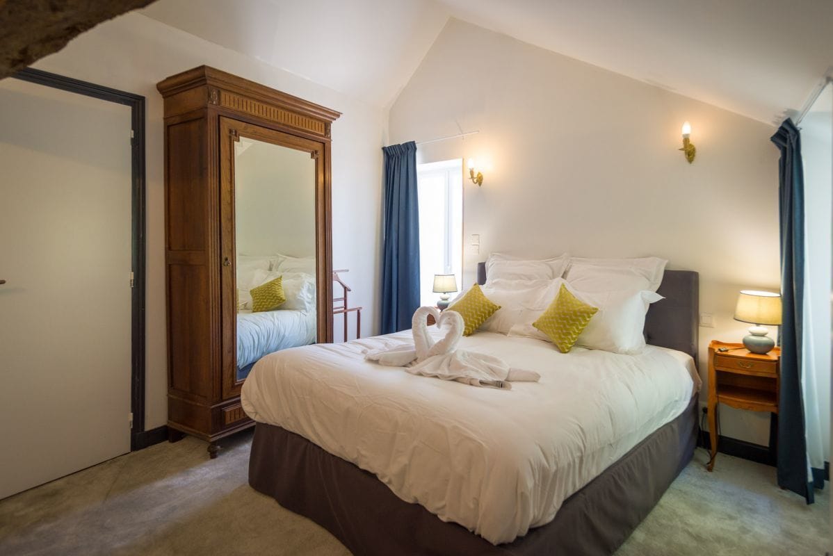 A bedroom with a large bed, a wardrobe, a mirror, a nightstand, and a lamp.