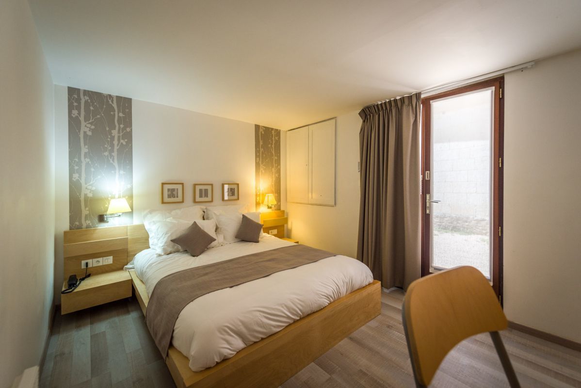 A hotel room with a bed, bedside tables, a chair, a wardrobe, and a sliding glass door to the outside.