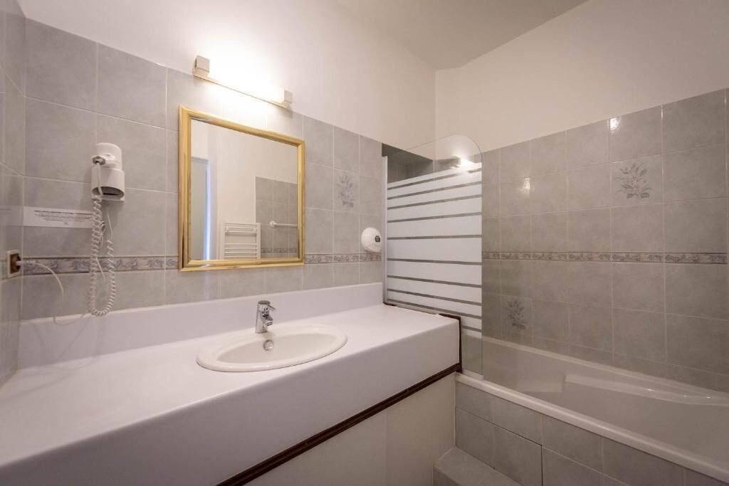 A bathroom with a white sink, a mirror with a gold frame, a hairdryer, and a shower area.
