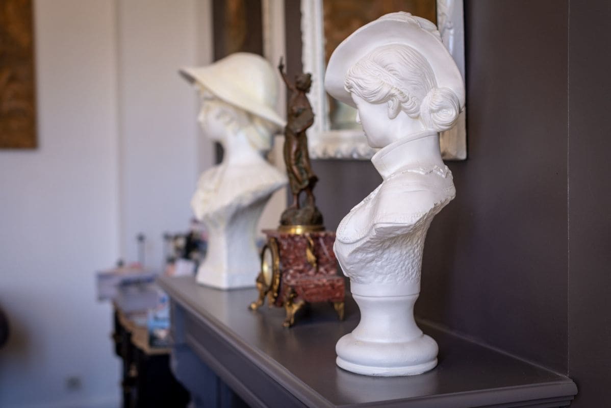 Una escultura de busto sobre una repisa con un espejo que refleja otro busto.