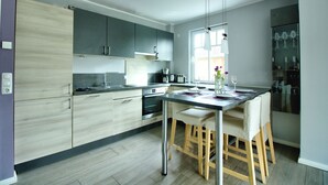 A modern kitchen with grey cabinets, a stainless steel sink, and a dining area with a table and chairs. - Carolin Dangast (Varel)