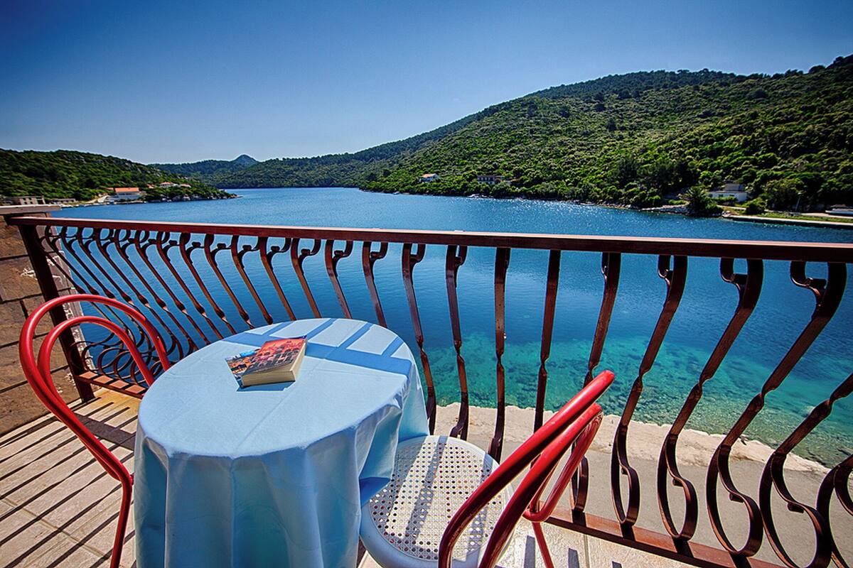 A deck with a table and chairs overlooking a lake with a mountainous backdrop.