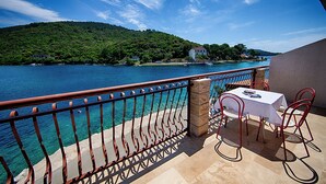 Un balcon avec une table et des chaises donnant sur une étendue d’eau et une colline.
