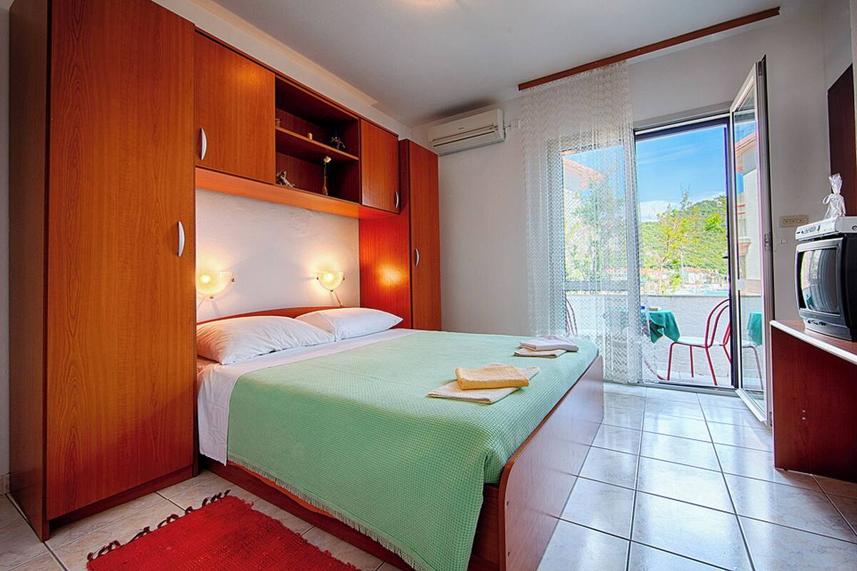 A bedroom with a bed, wooden wardrobe, and a balcony with a TV.