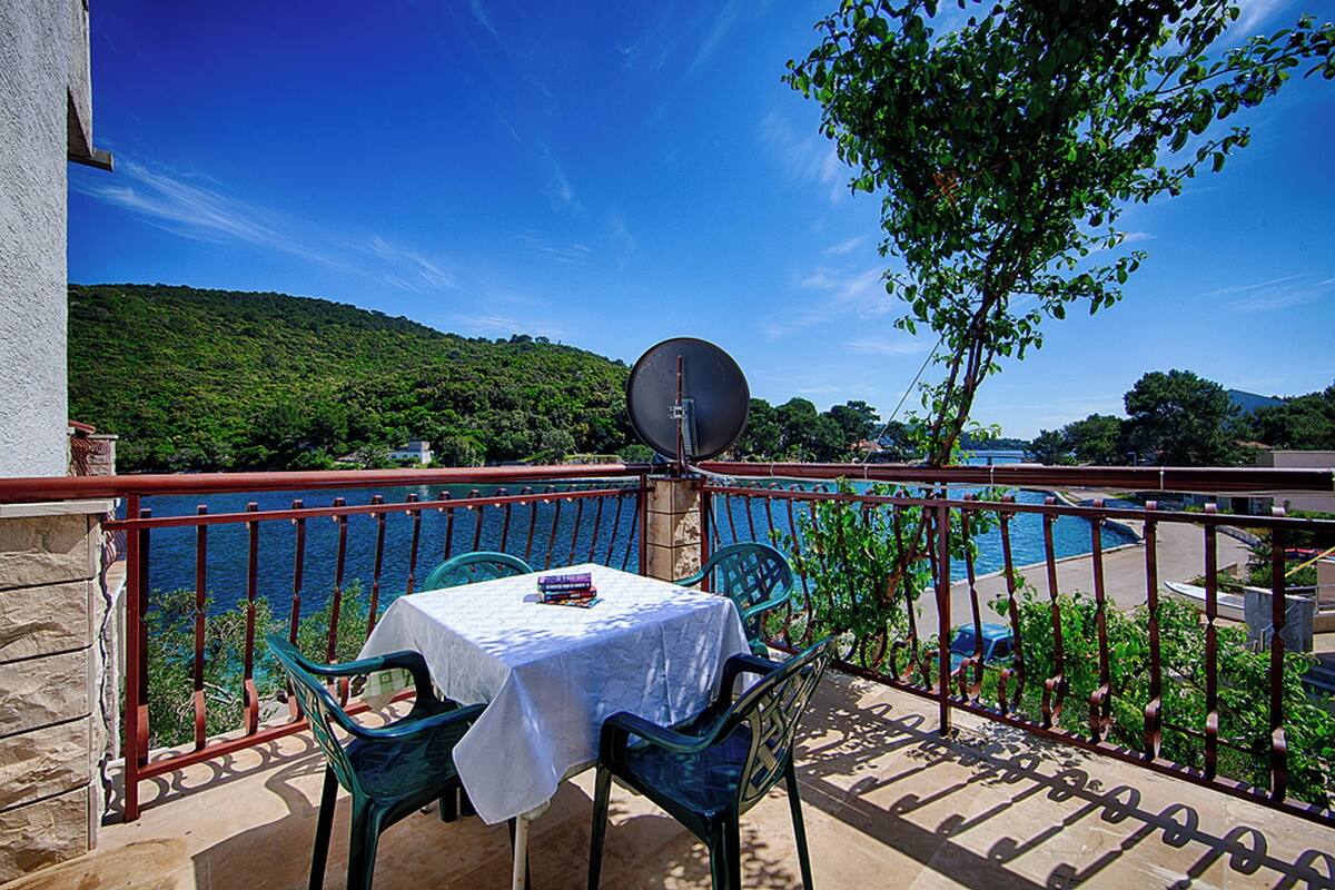A balcony with a table and chairs, overlooking a body of water and greenery.