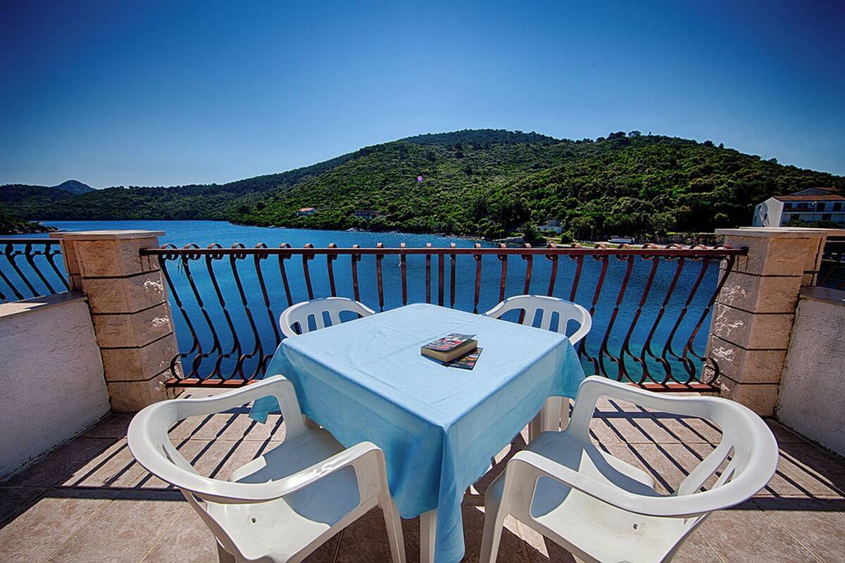 A terrace with a table and chairs, overlooking a body of water and a green hill.