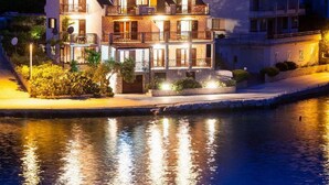 Une propriété à plusieurs étages située en bord de mer, dotée de balcons, d’une piscine et d’un éclairage extérieur soigné.