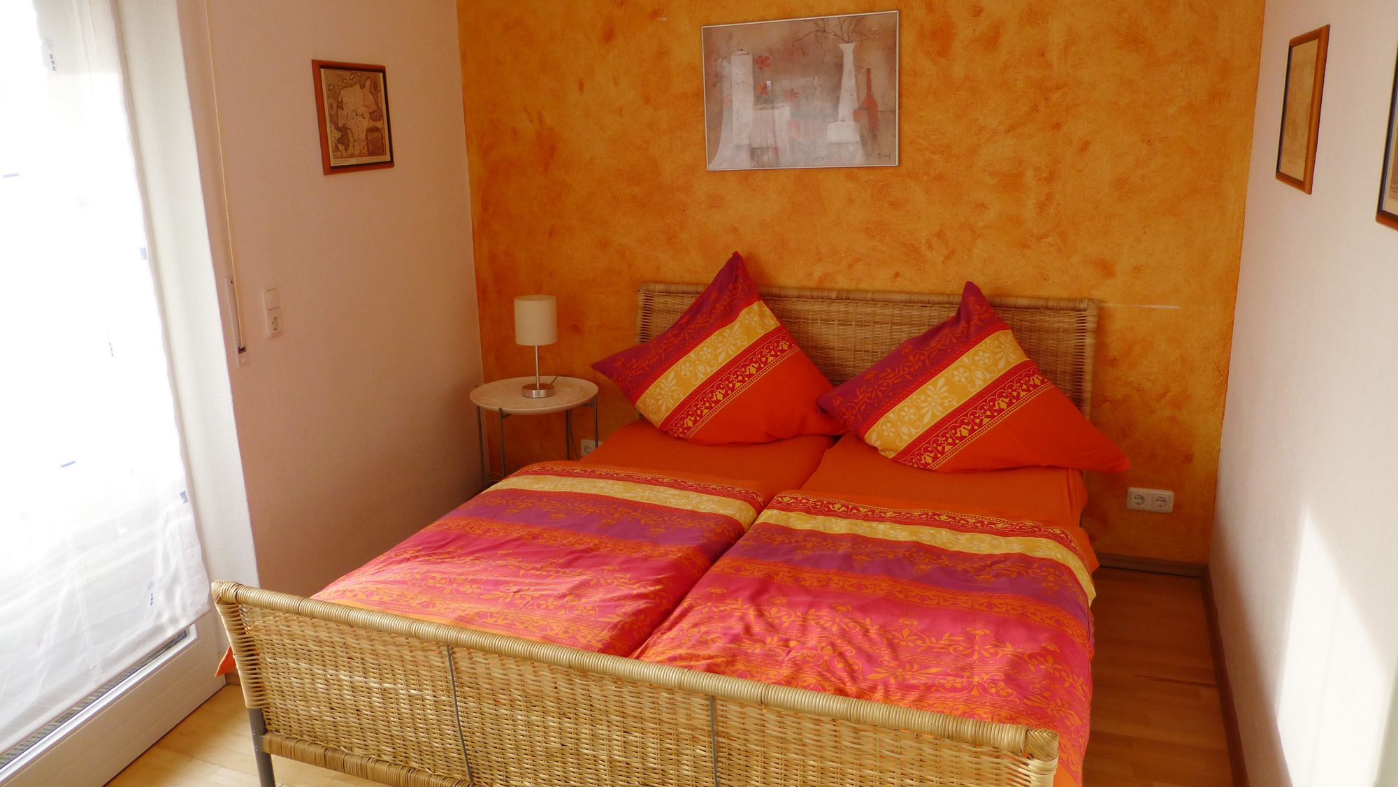Una stanza con un letto, un tavolino con una lampada e una sedia in vimini.