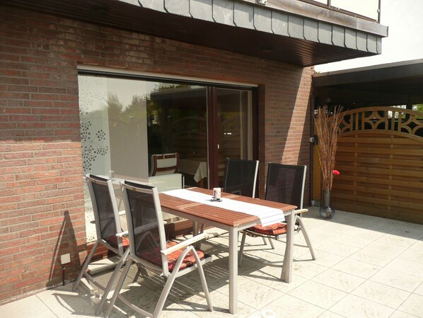 An outdoor patio with a table and chairs, a sliding glass door, and a wooden gate.