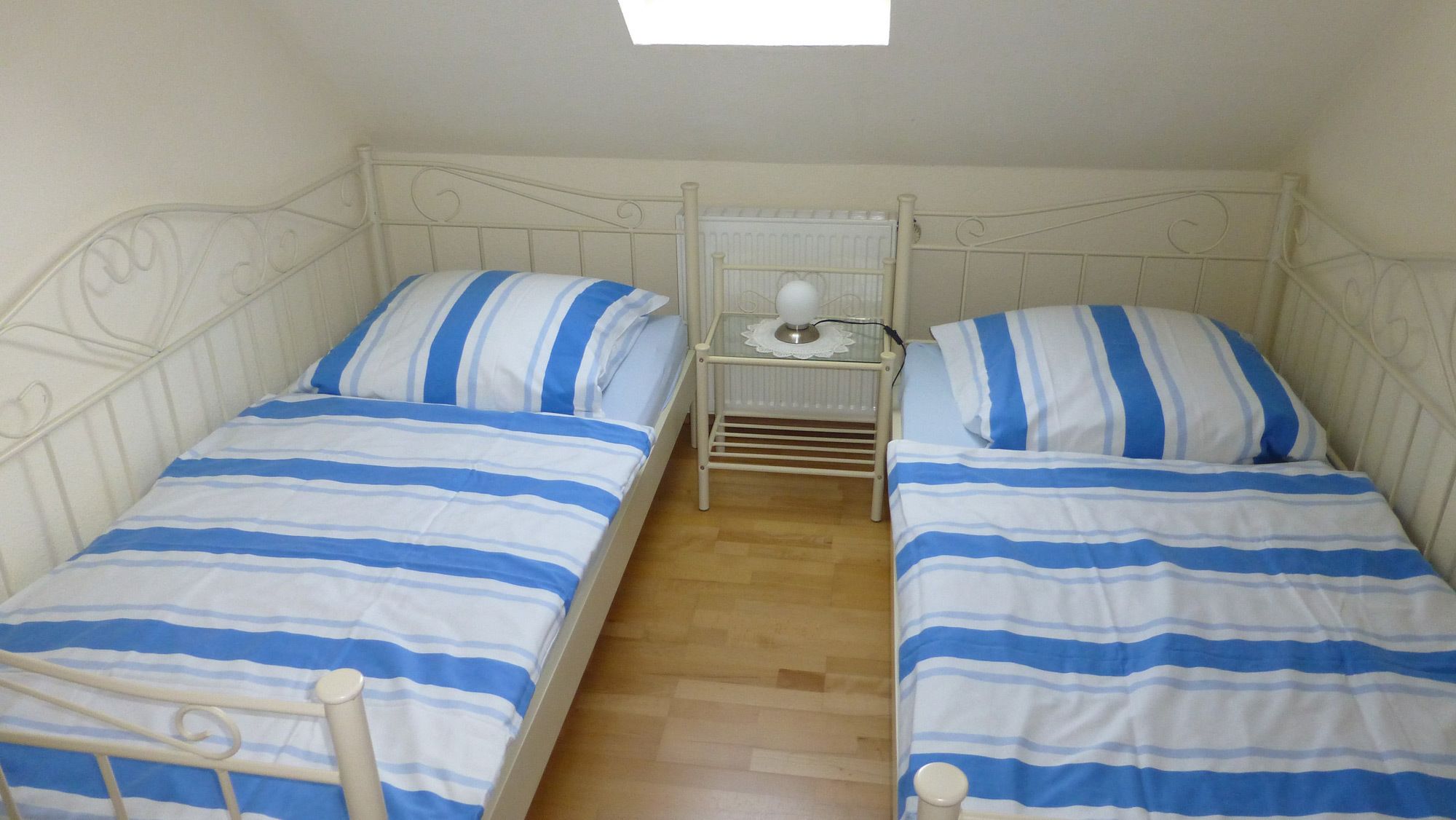 Een kleine, eenvoudige kamer met twee bedden, elk voorzien van blauw-wit gestreept beddengoed.