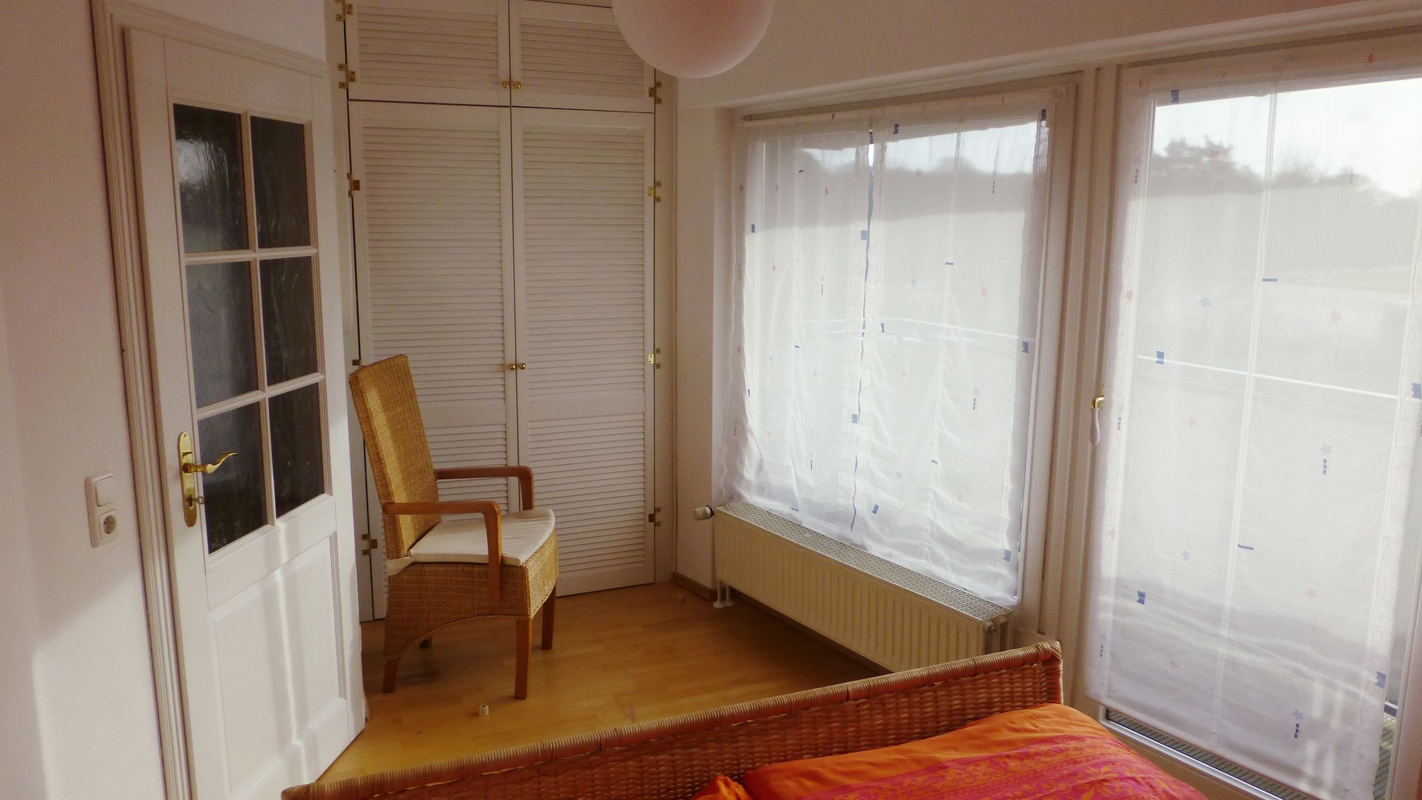 A room with a bed, a chair, a radiator, and a window with curtains.
