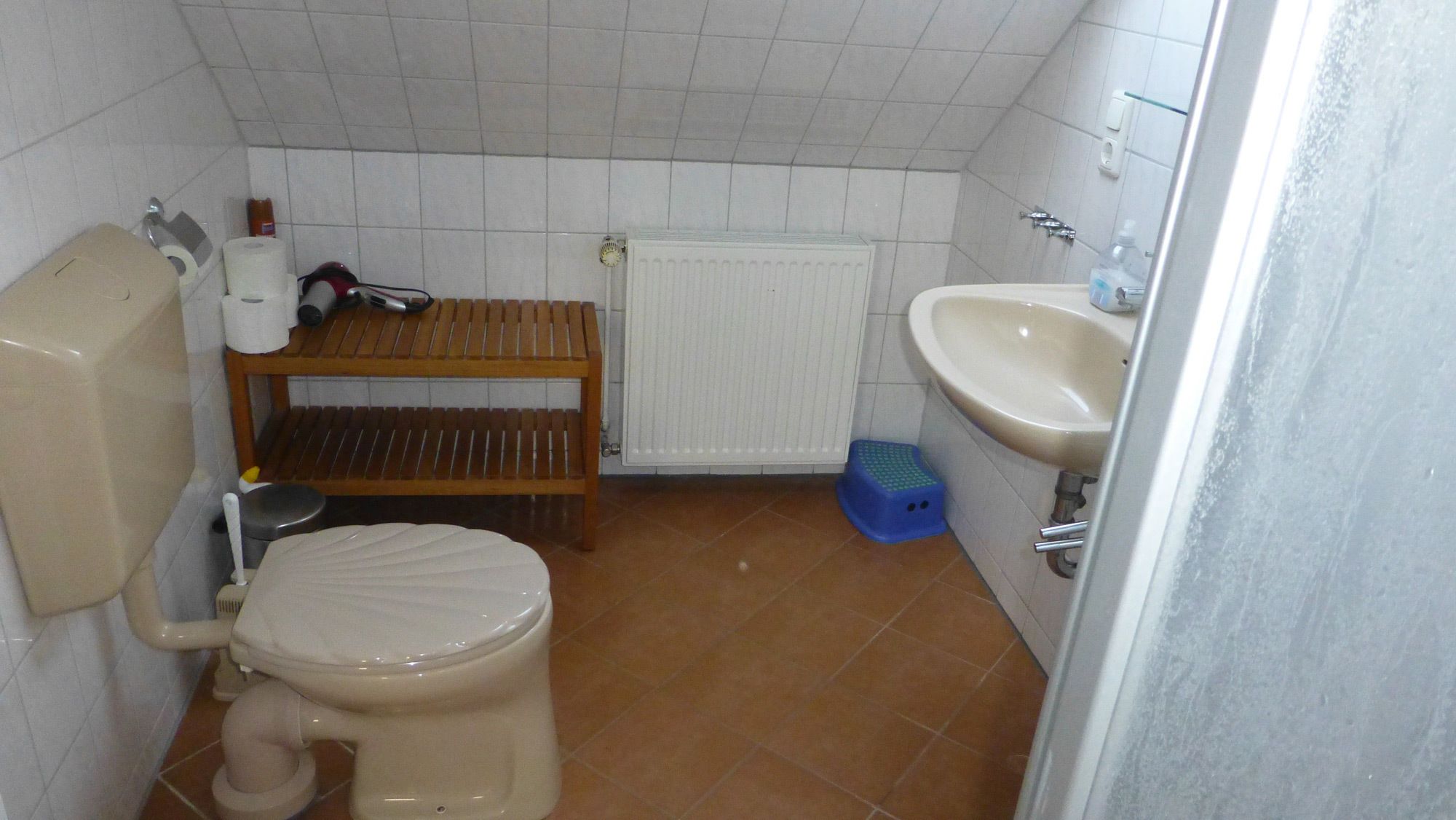 Un bagno piccolo con il water, uno scaffale di legno, un termosifone e un lavandino.