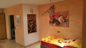 Een slaapkamer met een bed, een houten wijnrek, een wandplank en een schilderij van bloemen.